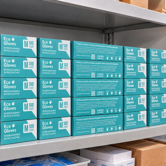 Eco Gloves biodegradable nitrile glove boxes neatly stacked on metal warehouse shelves, featuring turquoise packaging, medium size labels, and women-owned branding.