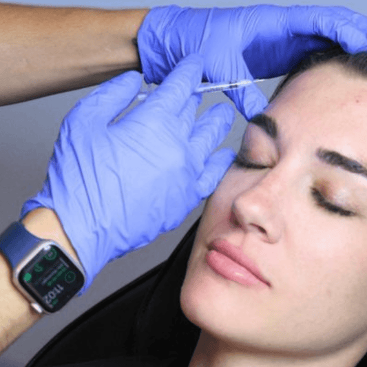 Medical professional wearing blue nitrile disposable gloves administering a cosmetic injectable treatment to a patient’s forehead.